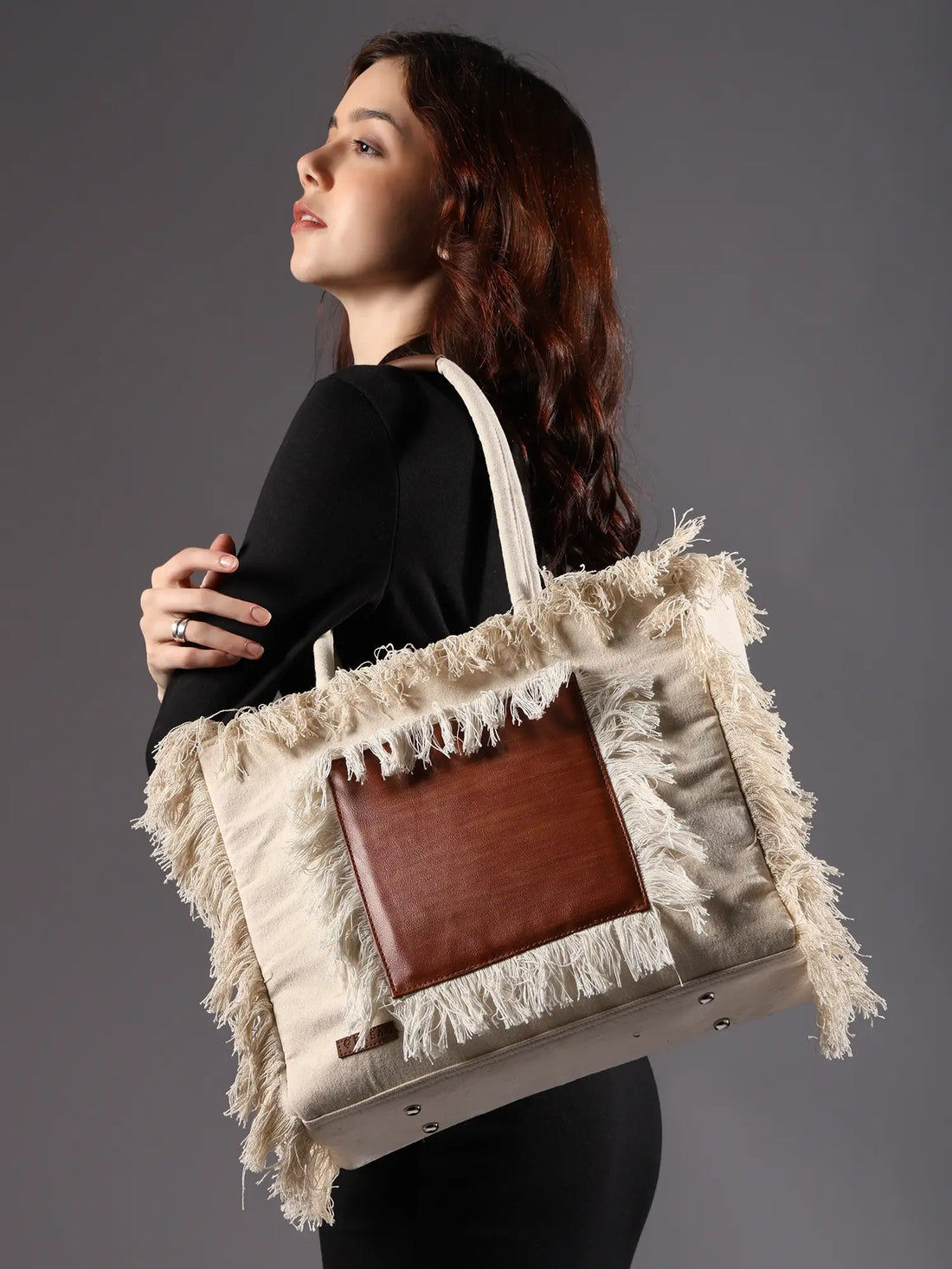 Beige tote bag with brown leather patch and fringes on a white background