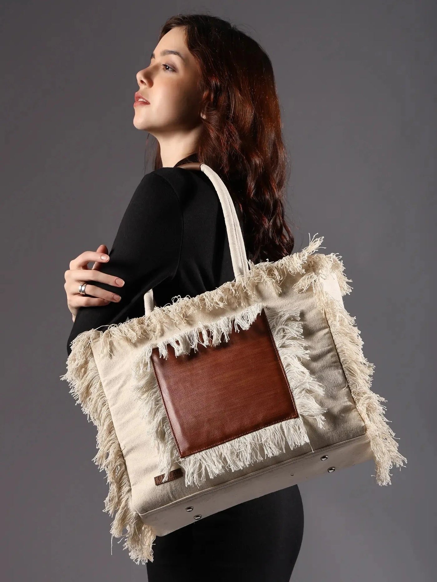 Woman holding a large tote bag with fringe details against a gray background by ENSAC