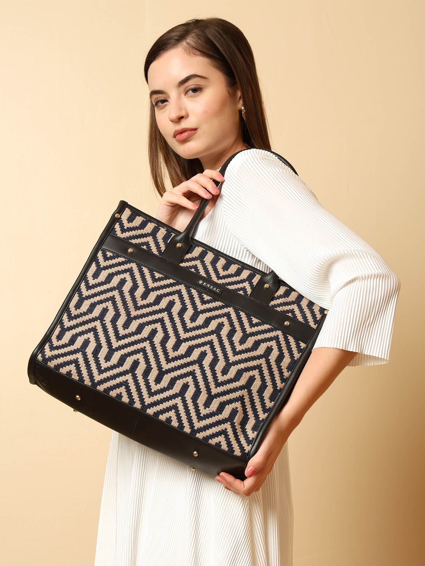 Woman holding a black and beige patterned handbag against a beige background  by ENSAC