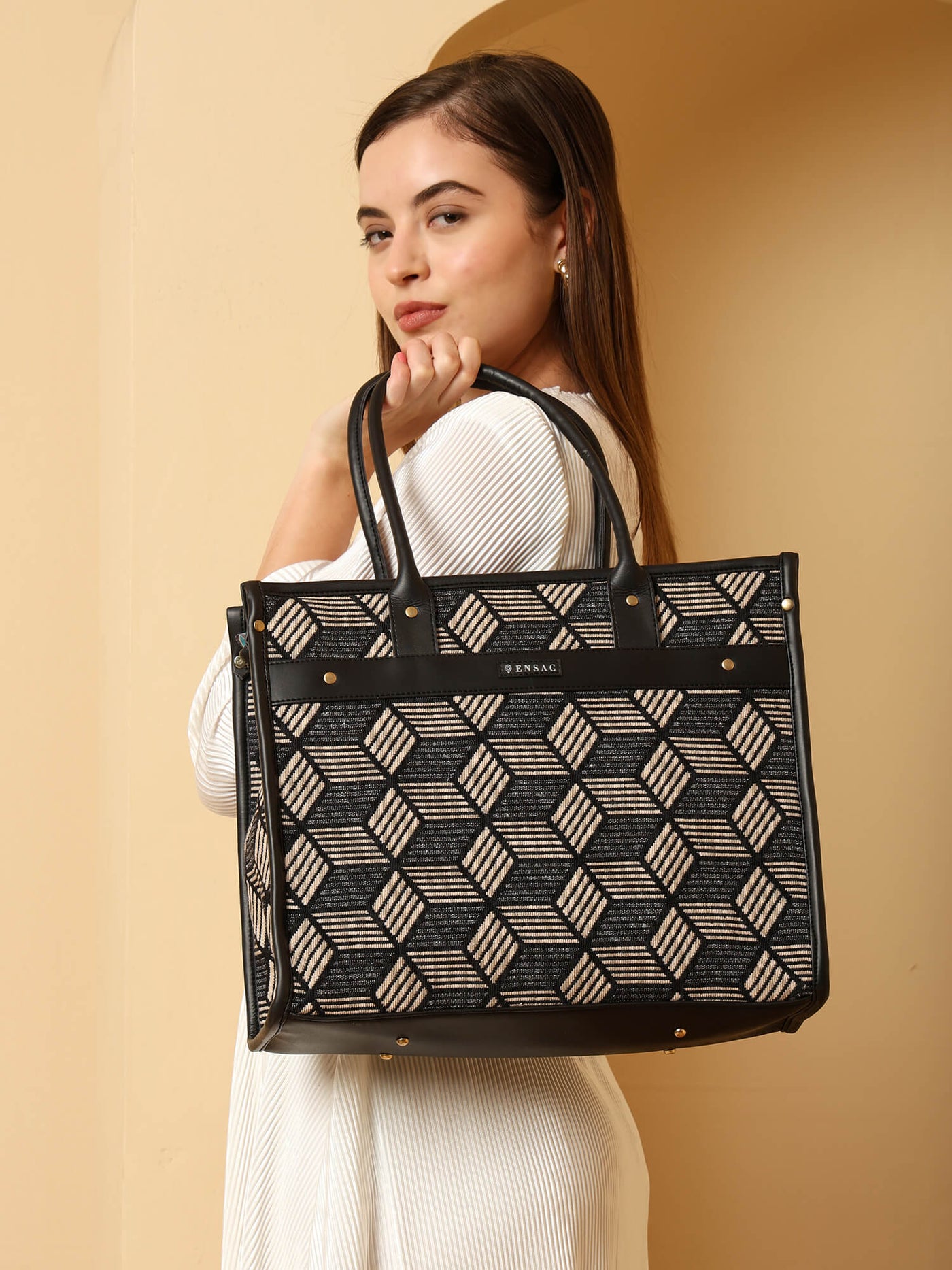 Woman holding a black and beige patterned handbag against a beige background  by ENSAC