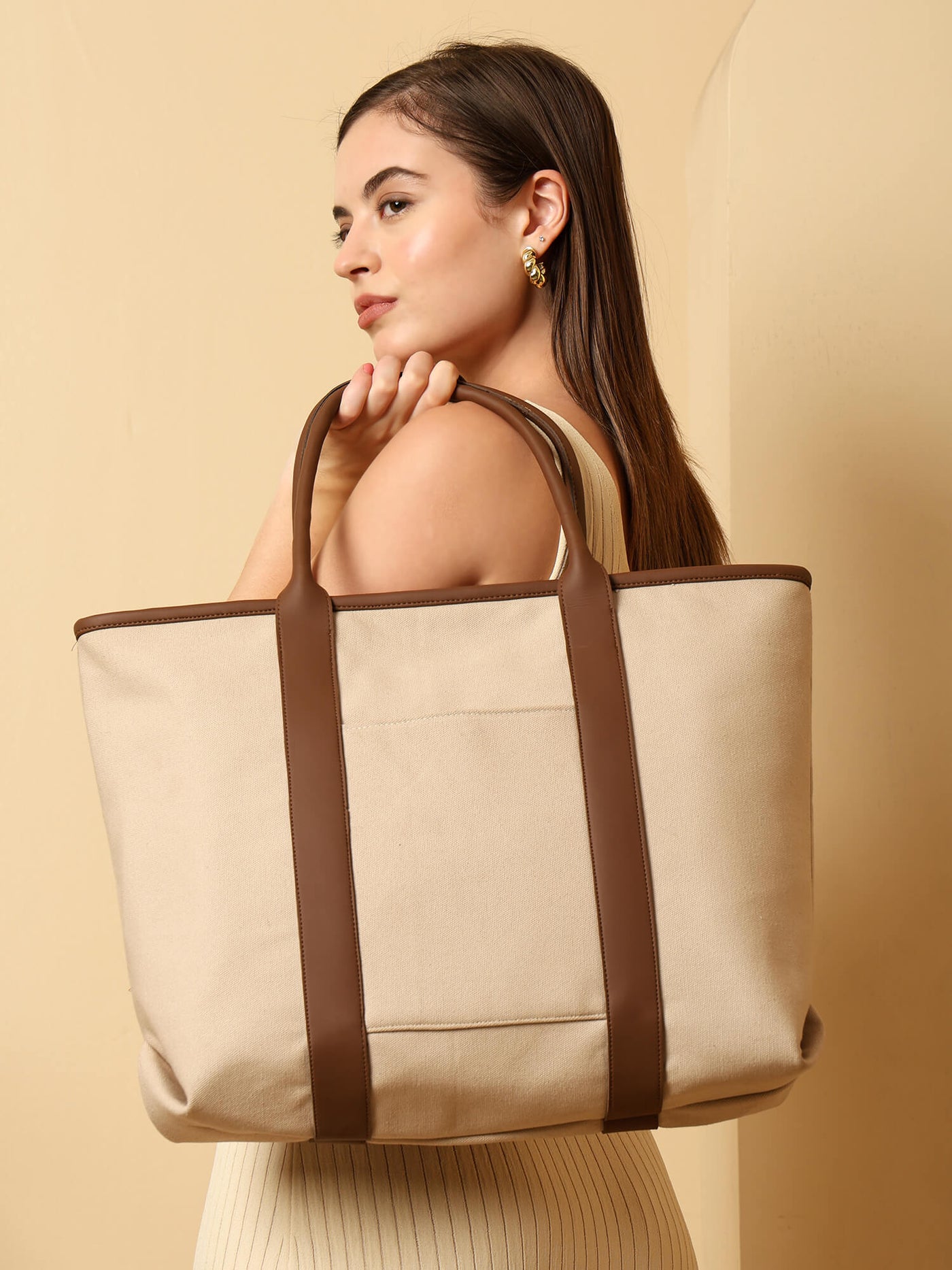 Woman holding a beige tote bag with brown straps against a beige background by ENSAC