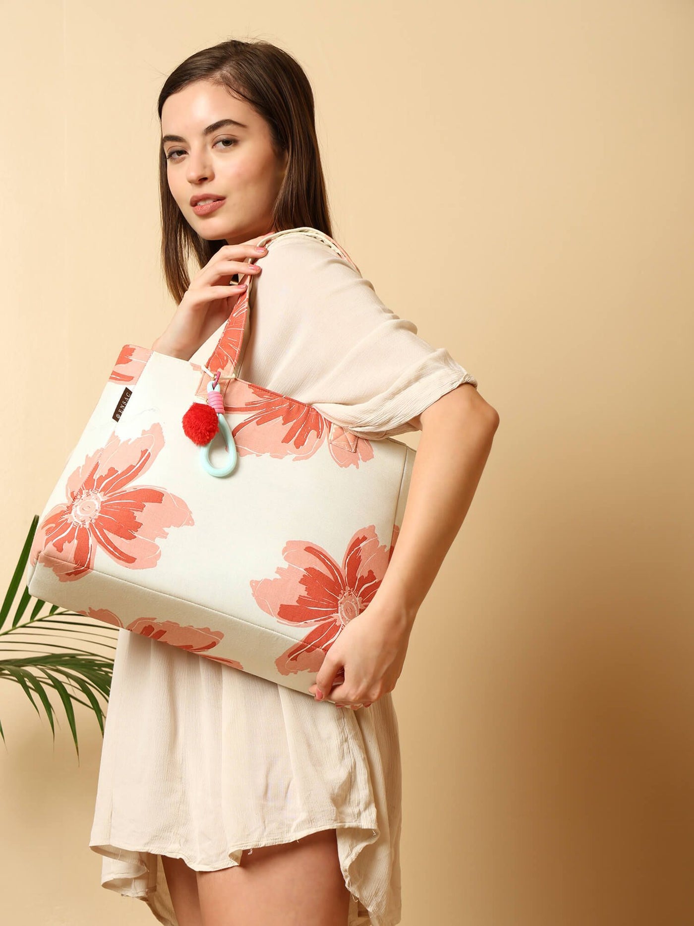Woman holding a tote bag with pink floral design against a beige background  by ENSAC