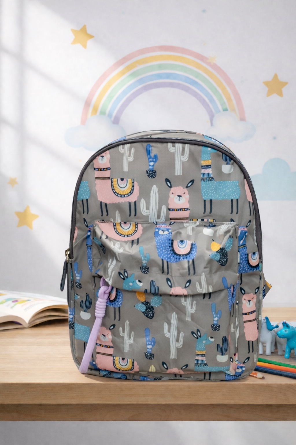 Backpack with llama and cactus pattern on a wooden surface with a colorful rainbow in the background BY ENSAC