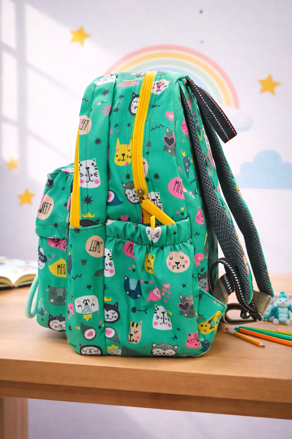 Green backpack with cat pattern on a wooden table with a rainbow and stars in the background BY ENSAC